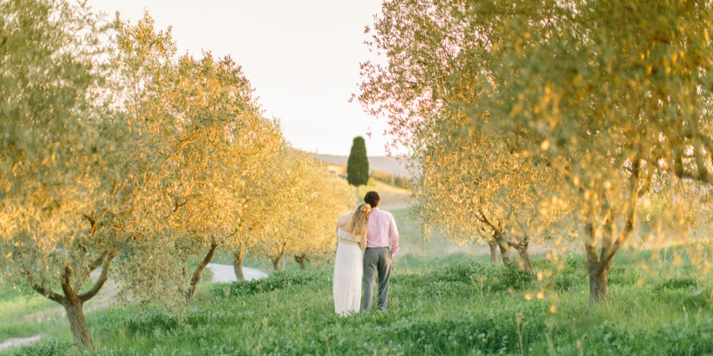 Wife leans on husband's shoulder in a grove of trees in Tuscany Italy