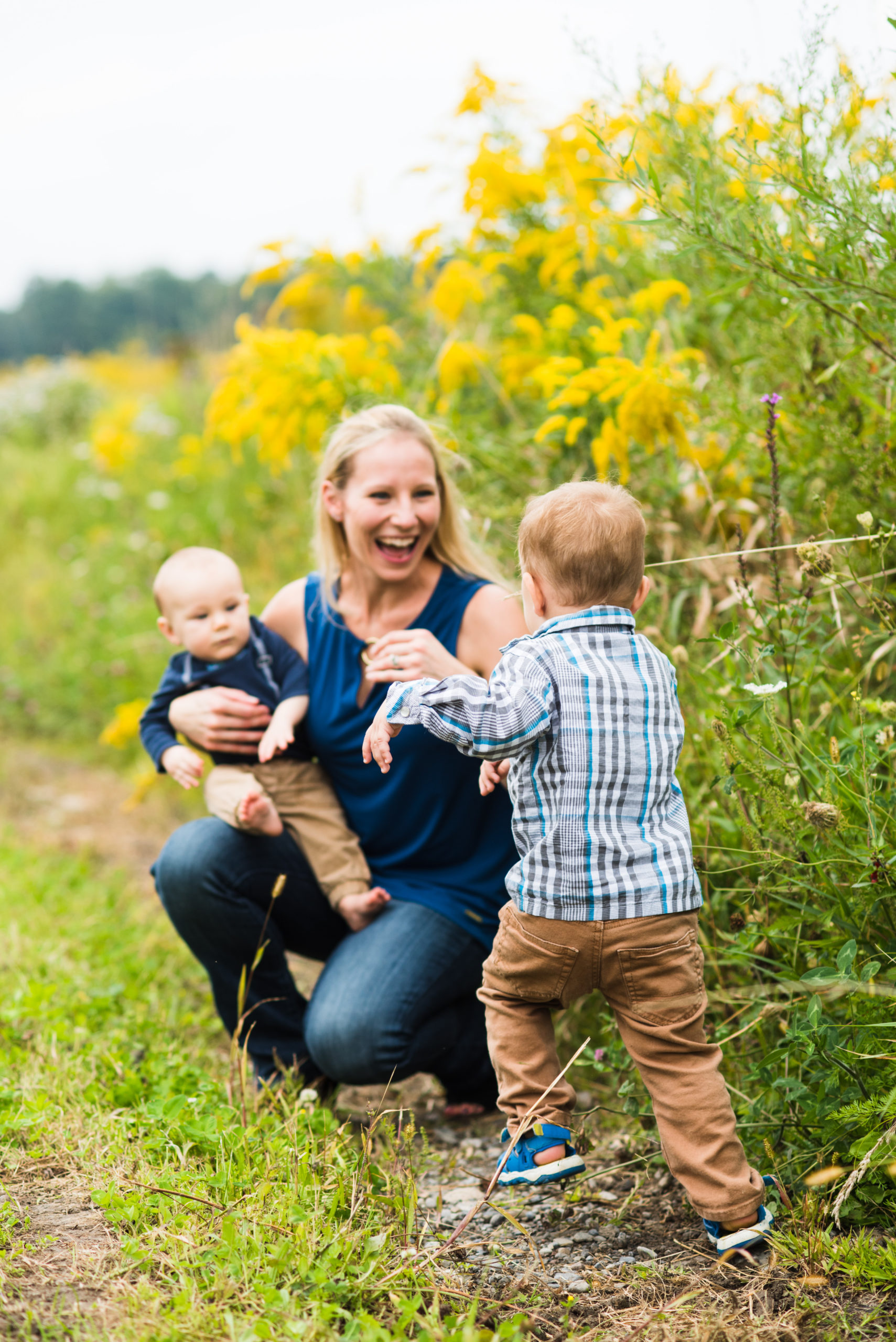 Syracuse wedding photographer H Hawkins Photography hugs and kisses her two little boys in a field after her miscarriages
