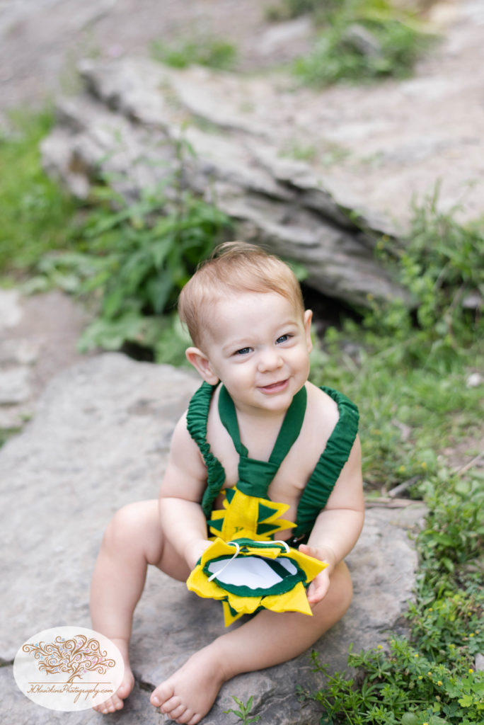 one year old in dinosaur birthday outfit sitting on a rock