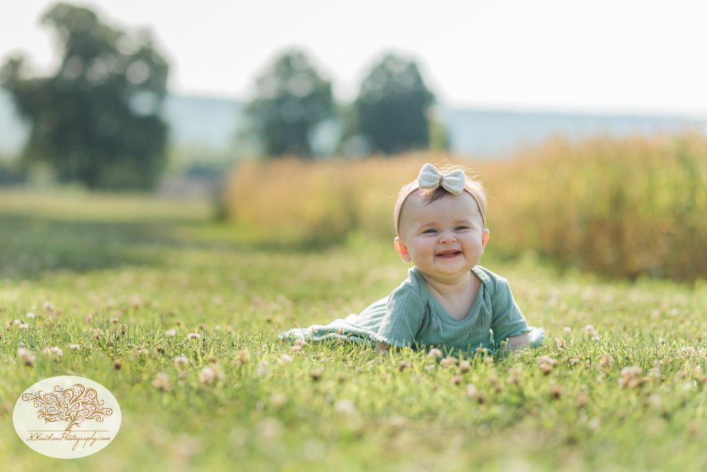 Baby girl lays on her tummy in the grass for her summer family pictures