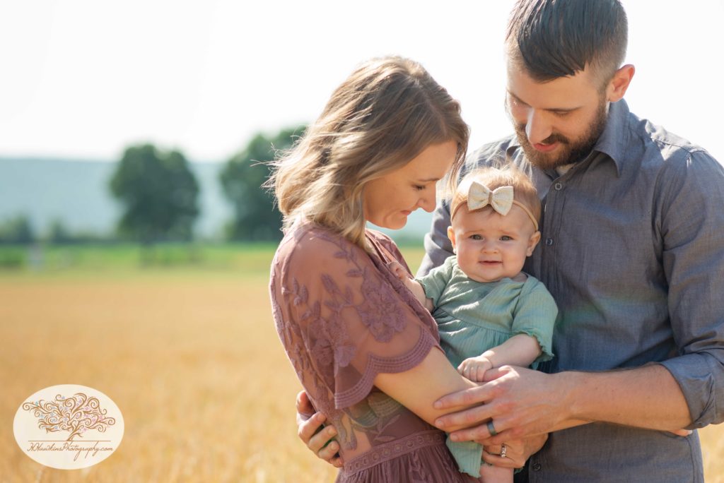 mom and dad look at baby in a wheat field during family pictures