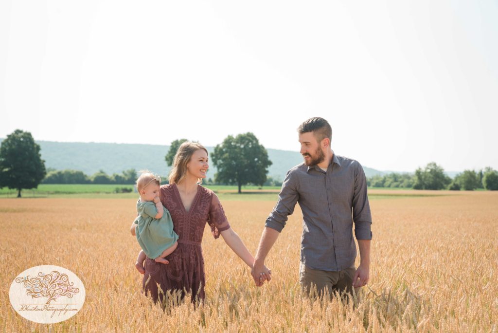 Husband and wife walk hand in hand through a wheat field in Syracuse during family pictures