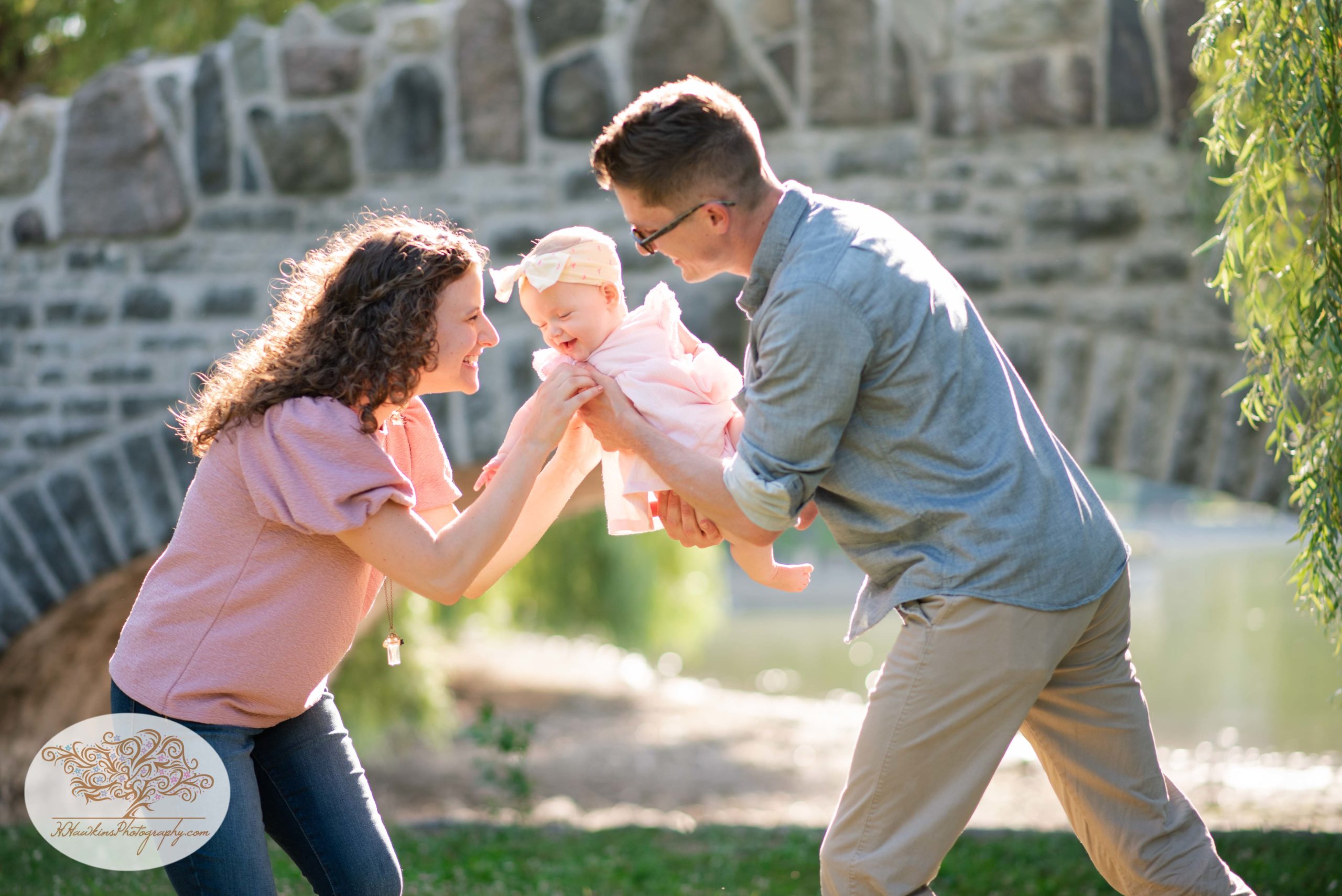 Mom and dad tickle baby girl at Upper Onondaga Park in Syracuse NY while family photographer takes their picture