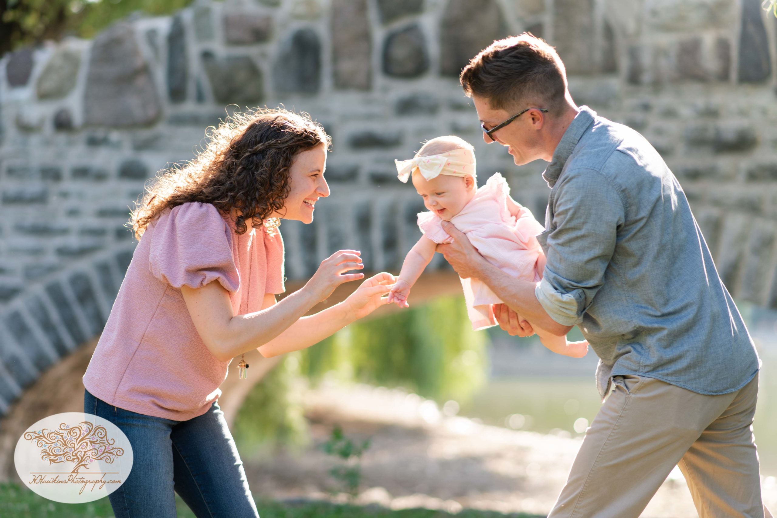 Mom and dad tickle baby girl at Upper Onondaga Park in Syracuse NY while family photographer takes their picture