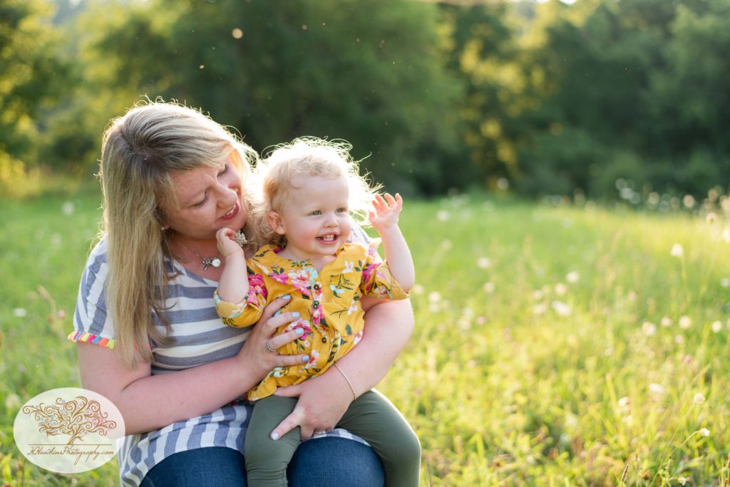 Mom holds her little girl on her lap in a field of summer flowers in Syracuse NY for their family pictures