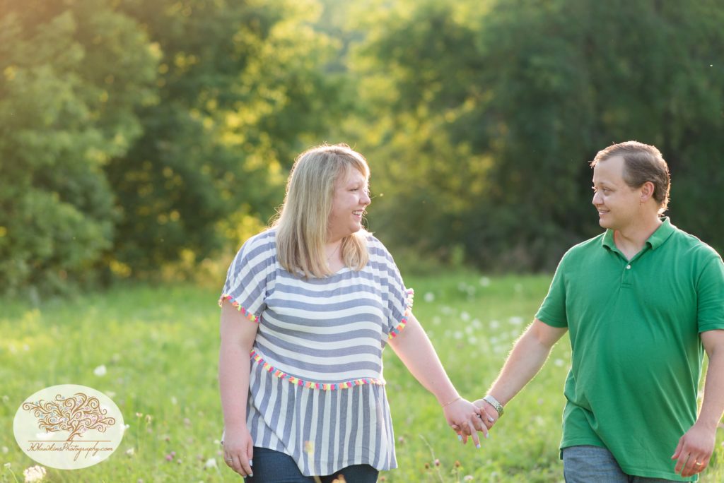 Husband and wife walk hand in hand through a summer field in Camillus NY during their family picture session