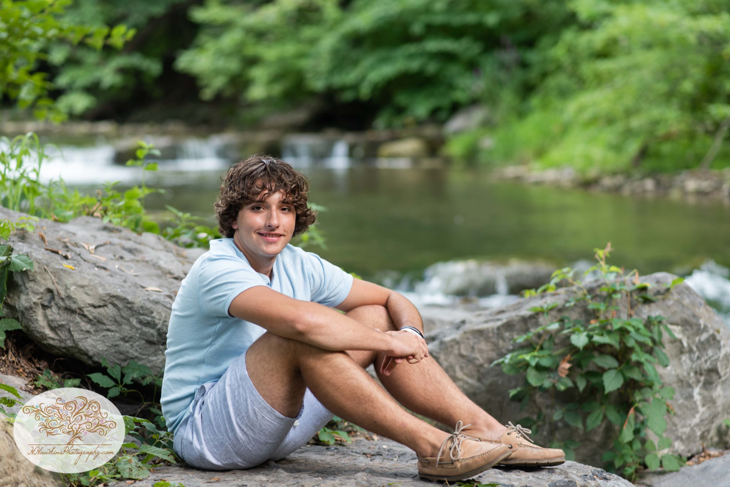 Syracuse high school senior sits on a rock smiling at the camera in front of Nine Mile Creek in Marcellus NY