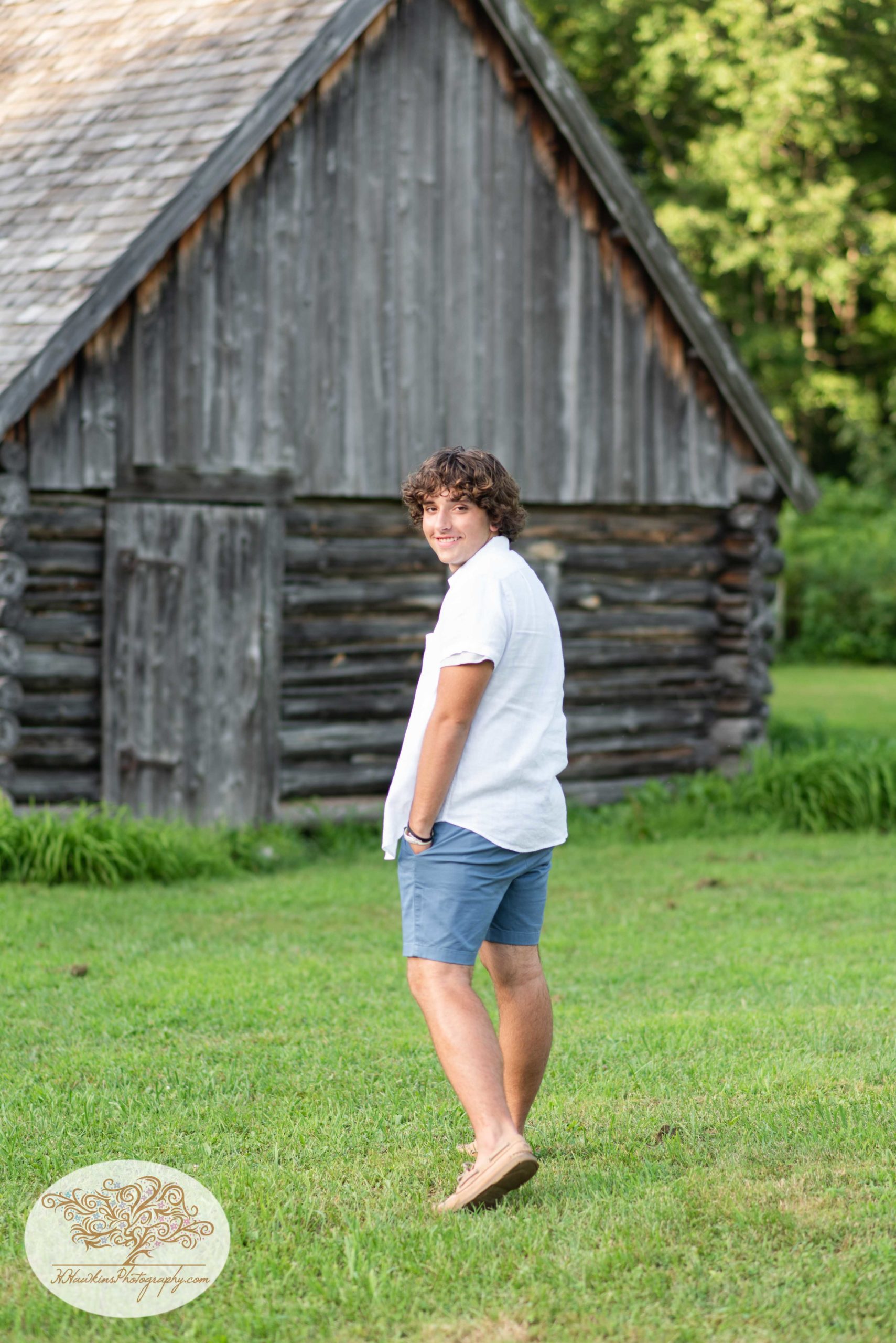 Syracuse high school senior looks over his shoulder as he walks towards log cabin at Baltimore Woods during his pictures