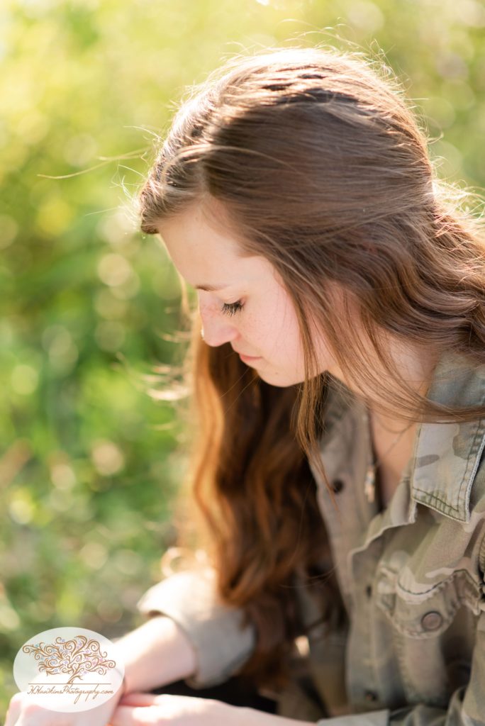 CNY Senior Pictures of a girl in a camo jacket with sunlight kissing the back of her head and brown hair falling over her shoulders
