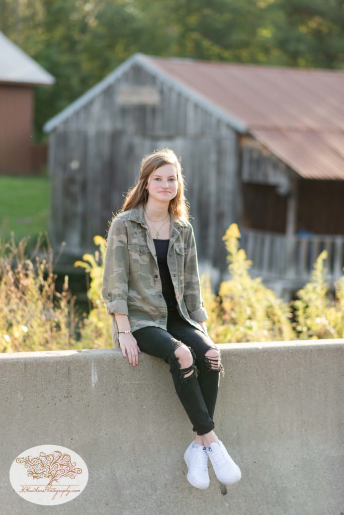 High school senior girl sits on a concrete barrier near the Erie Canal in Camillus NY for her CNY Senior Pictures session