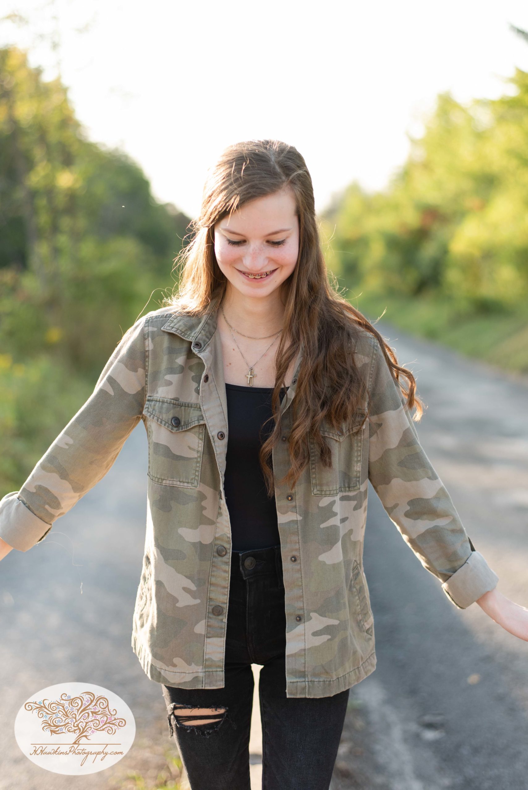 High school senior girl stands on concrete barrier near the Erie Canal in Camillus NY in black jeans and a camo jacket