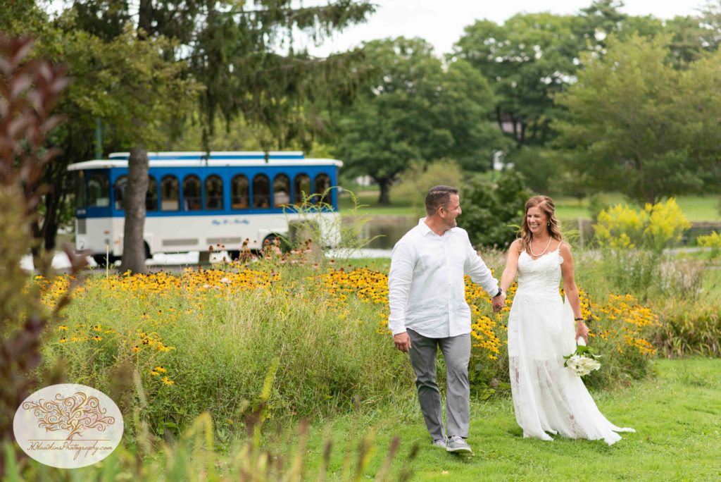 Groom leads bride through Hoopes Park in Auburn NY with Big D's limo trolley in the background