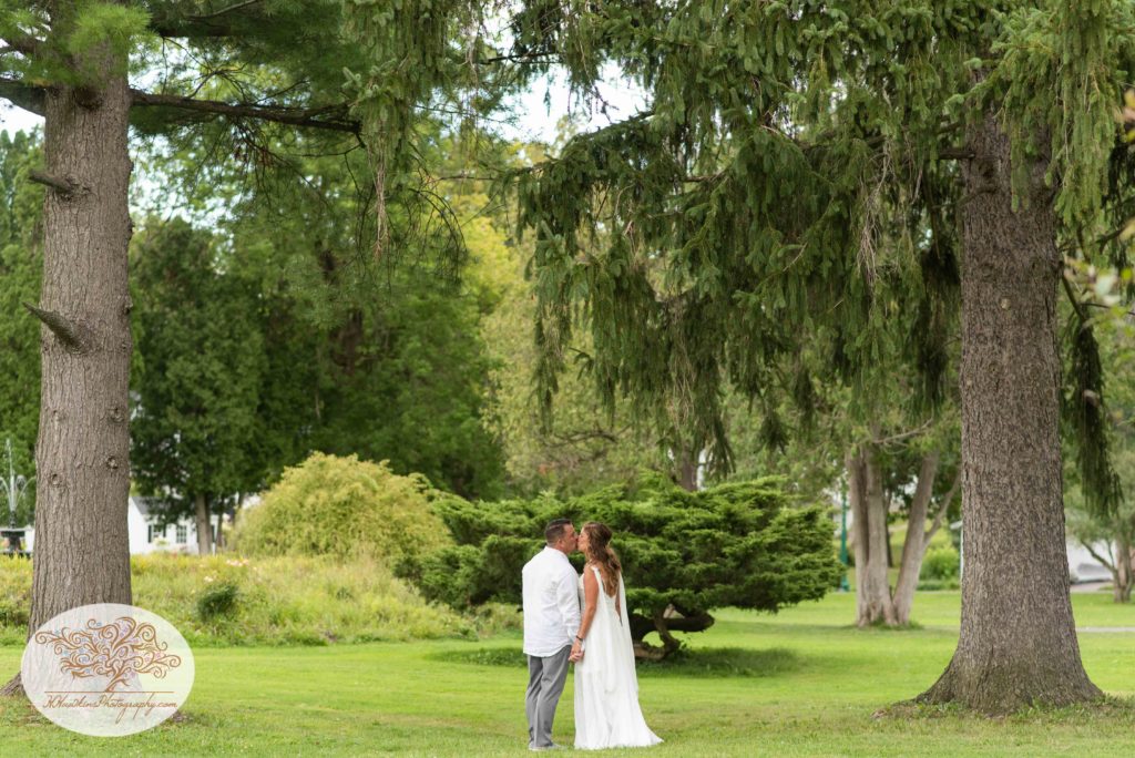 Bride and groom stand between two large pine trees in Hoopes Park Auburn NY during their fingerlakes wedding
