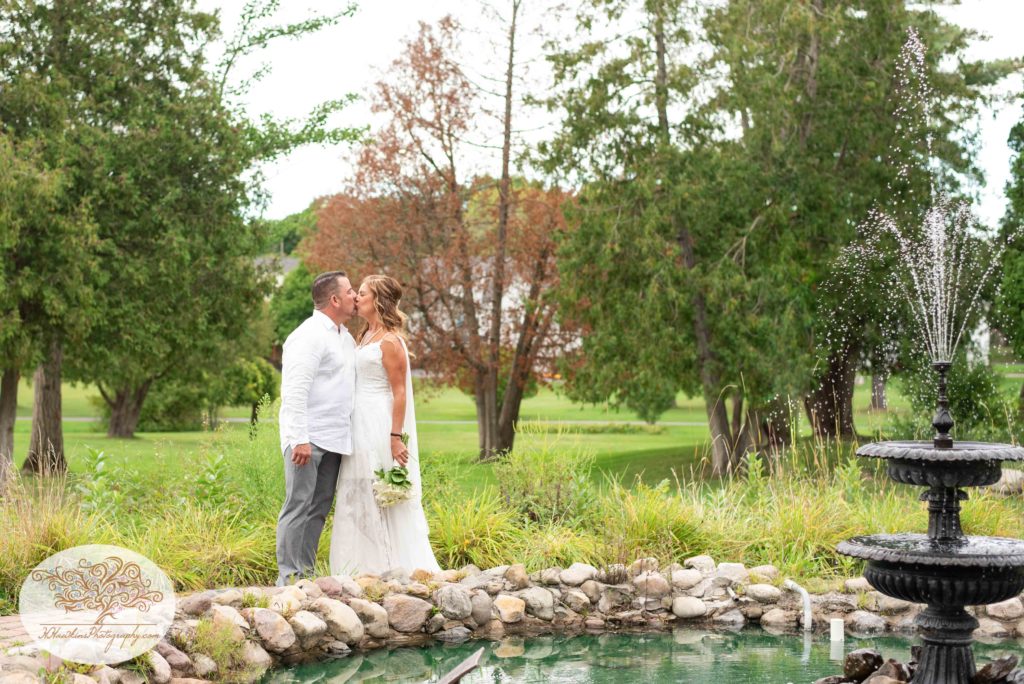 Bride and groom stand in front of small fountain at Hoopes Park in Auburn NY by Fingerlakes Wedding Photographer