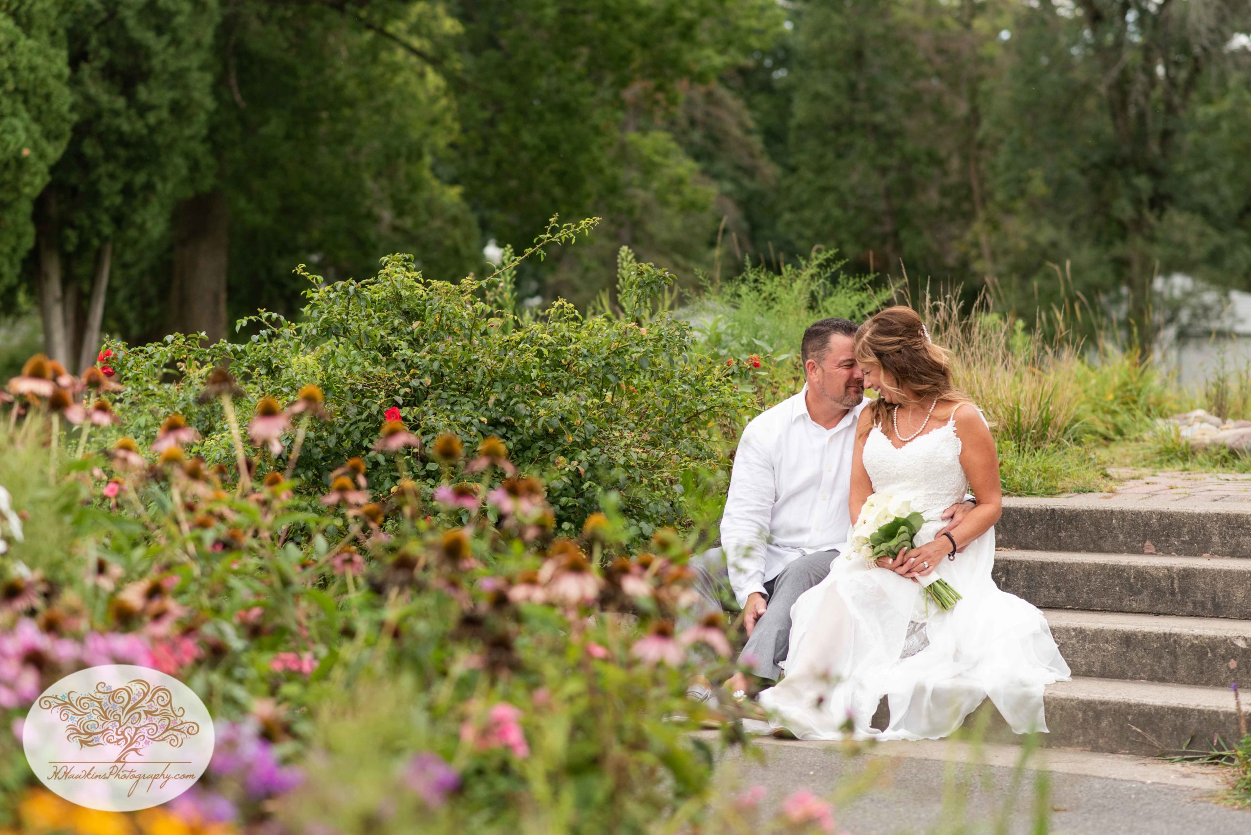 Bride and Groom sit on steps at Hoopes Park in Auburn NY with flowers surrounding them
