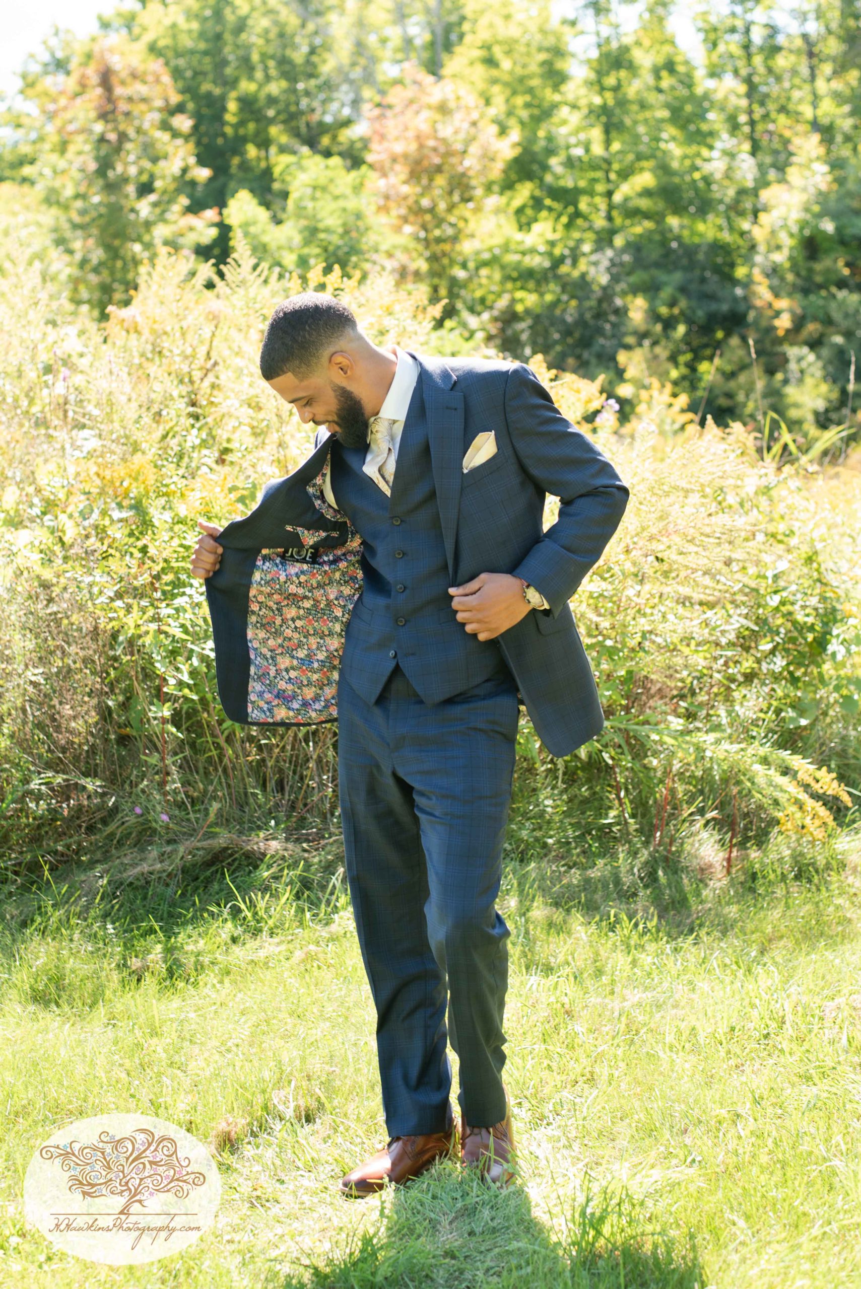 Groom and his custom made suit jacket in a field with sunshine behind him