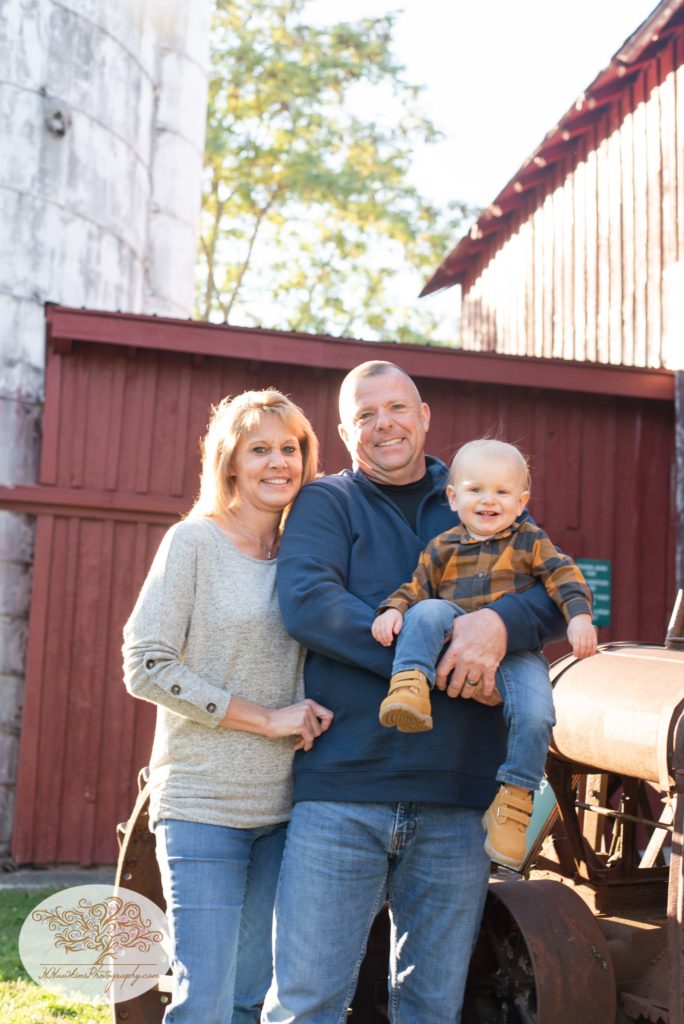 Grandma, Grandpa and Grandson captured by Syracuse family photographer at GIllie Lake in front of barn and silo and tractor