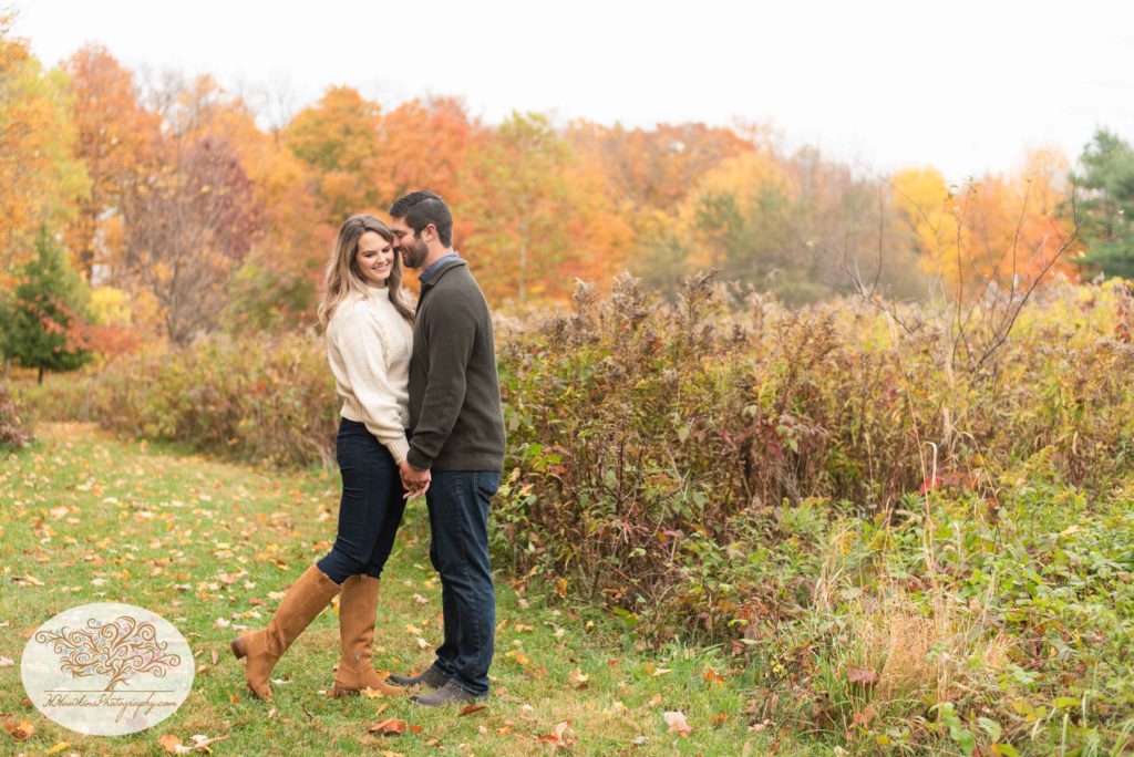 Groom whispers a secret in bride's ear as they hold hands during their syracuse fall engagement pictures at Baltimore Woods Marcellus NY
