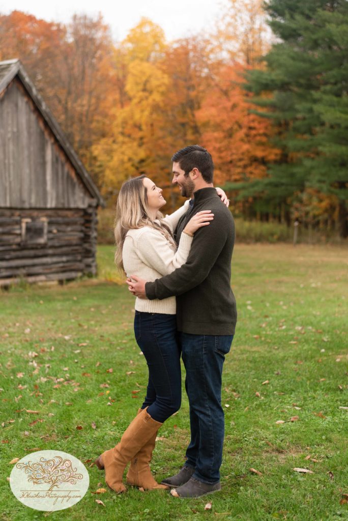 Bride looks at groom and as they stand together in front of the log cabin at Baltimore Woods in Marcellus NY for their Syracuse fall engagement pictures