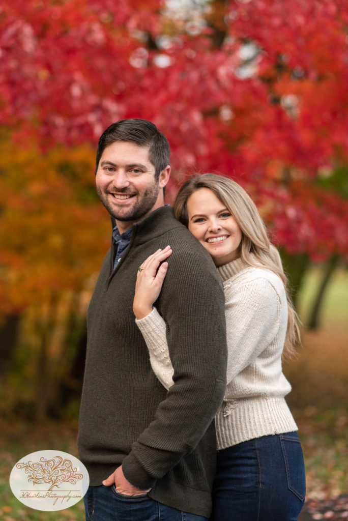 Bride and groom to be stand in front of red autumn tree at Marcellus NY for their Syracuse fall engagement pictures