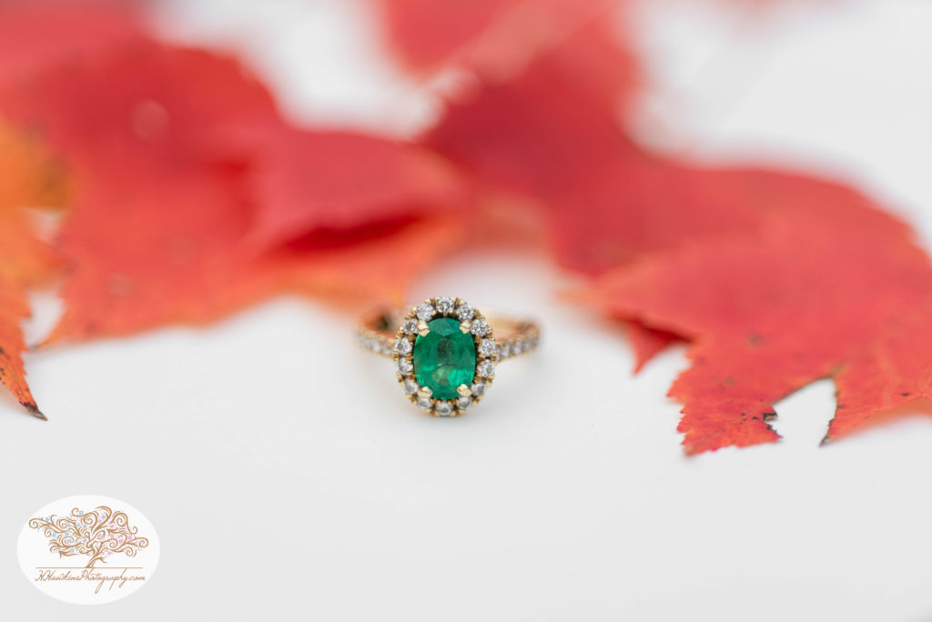 Emerald engagement ring set among red autumn leaves by Syracuse wedding photographer for their fall engagement pictures