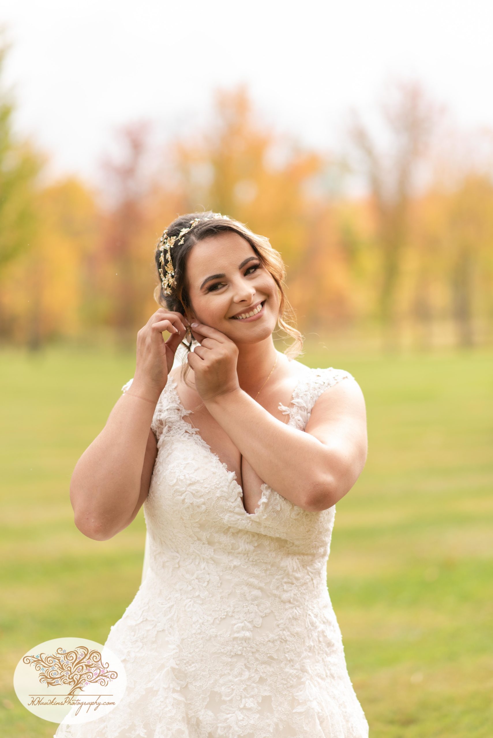 Bride puts her earrings in on her wedding day with fall foliage behind at Upstate NY barn wedding venue