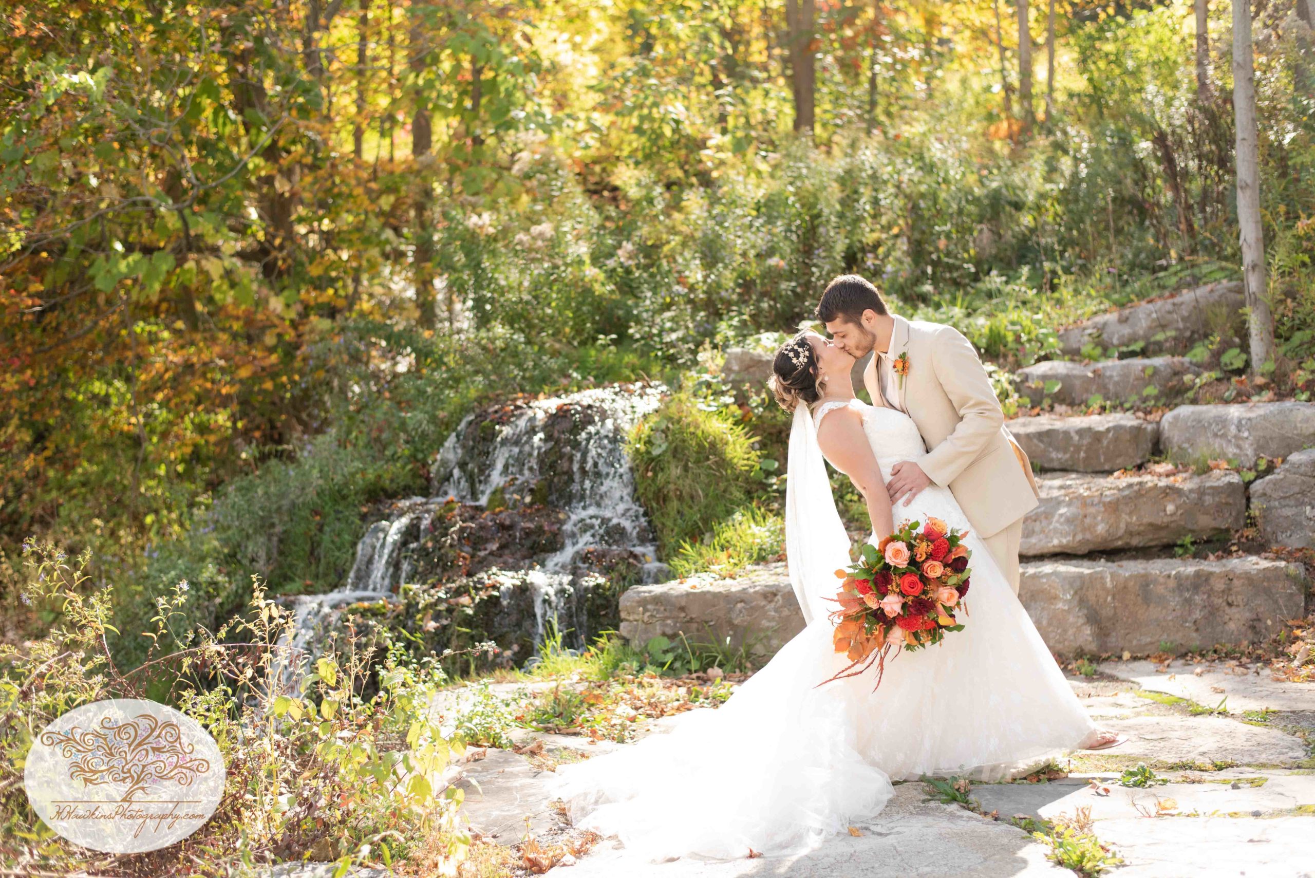 Groom dip kissing his bride in front of waterfall at Upstate NY barn wedding venue Wolf Oak Acres