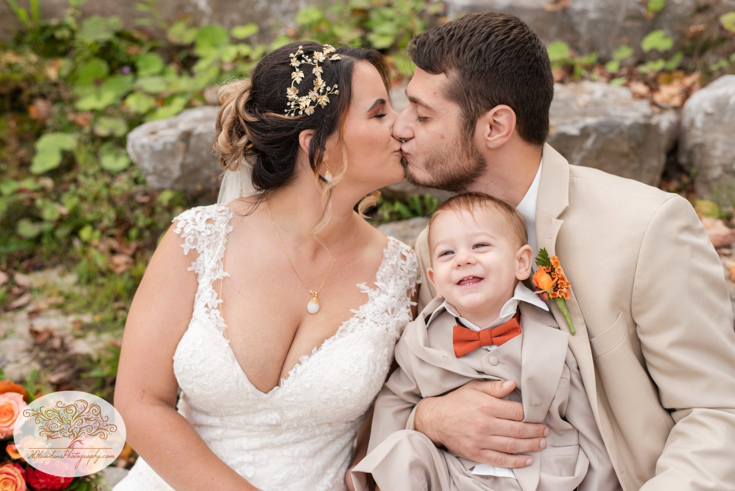 Bride and groom kiss while their son smiles up at the camera