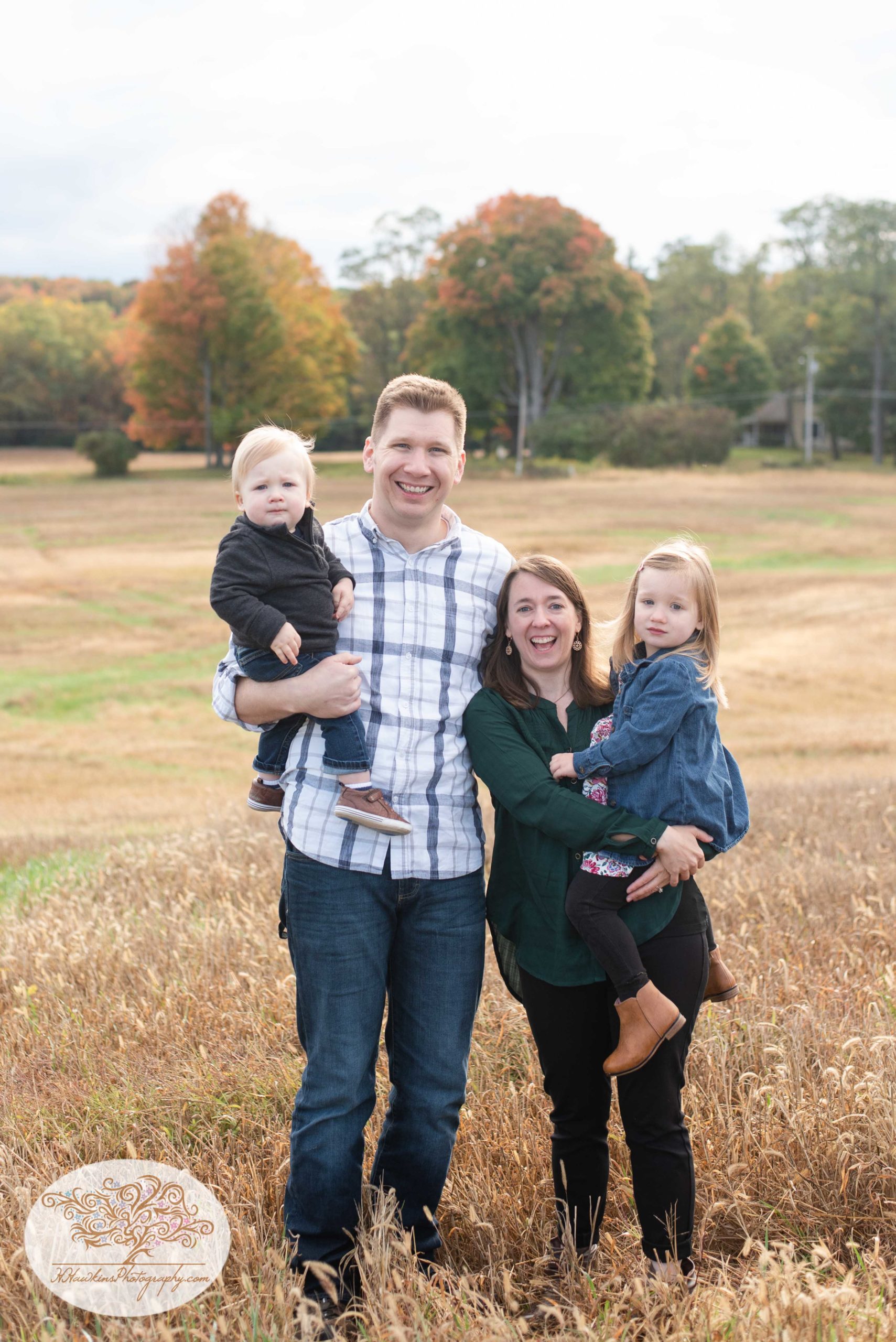 Family of four stand in a wheat field at Gillie Lake in CAmillus NY during their Upstate NY fall family pictures