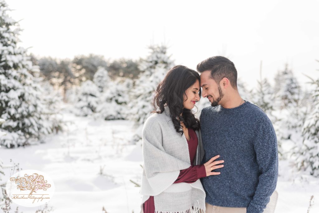 Bride and groom to be stand in the snow at a Christsmas Tree Farm at Critz Farms in Cazenovia for their engagement photos