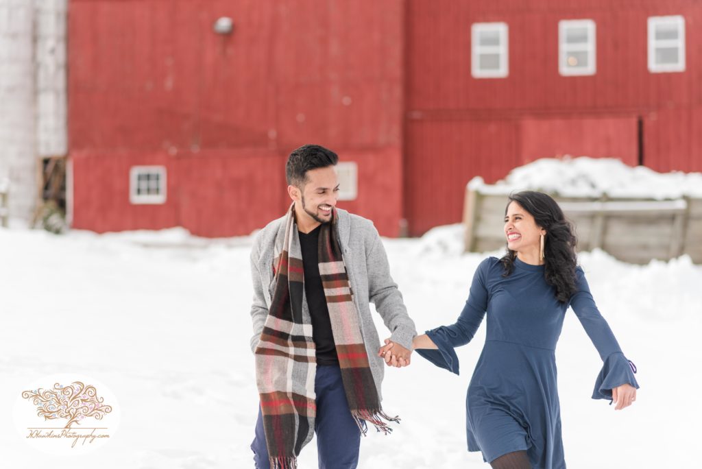 Bride and groom to be walk hand in hand during their snowy engagement pictures at Critz Farms in Cazenovia NY