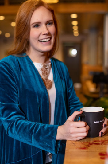 Courtney of Crown Coordination smiles as she stands at a coffee bar holding a mug