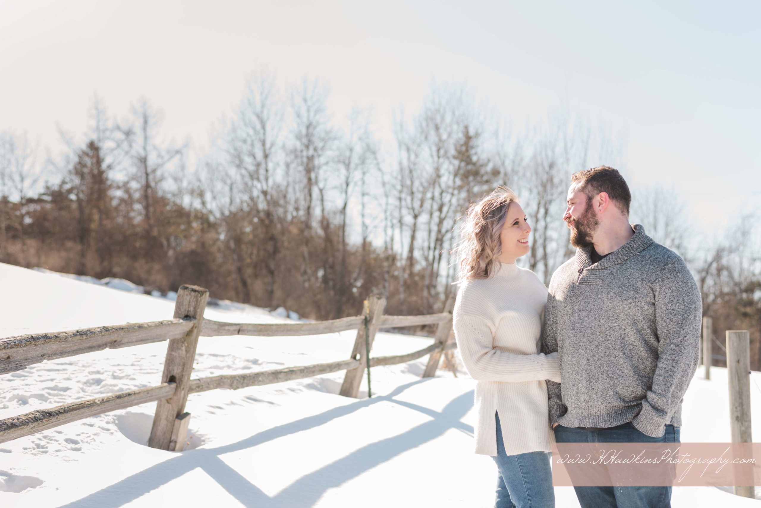 Bride and groom smile at each other standing in front of fence at Highland Forest during their engagement photo session by Syracuse wedding photographer