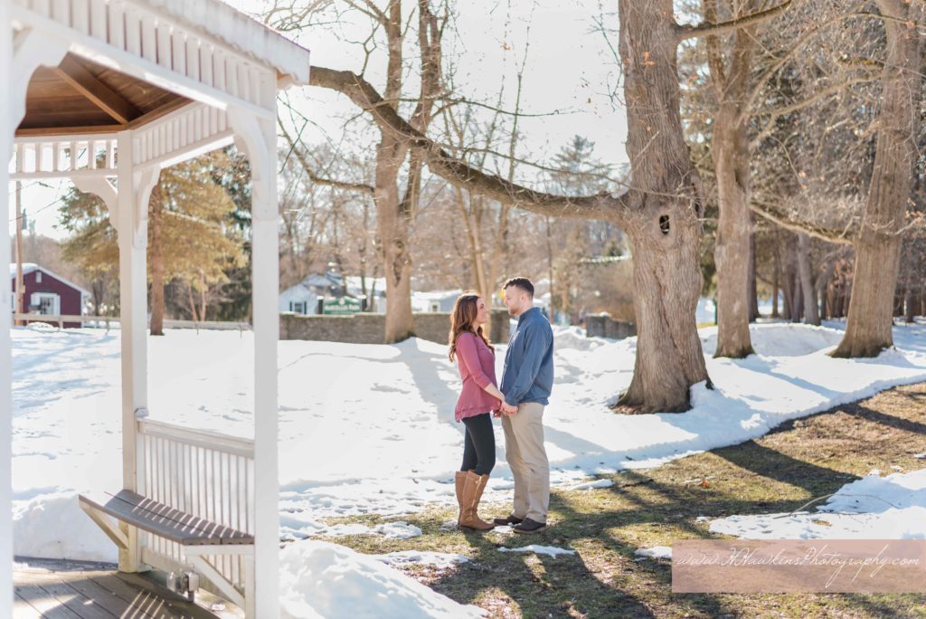 Bride and groom stand near gazebo at Marcellus Park during their engagement session in the snow