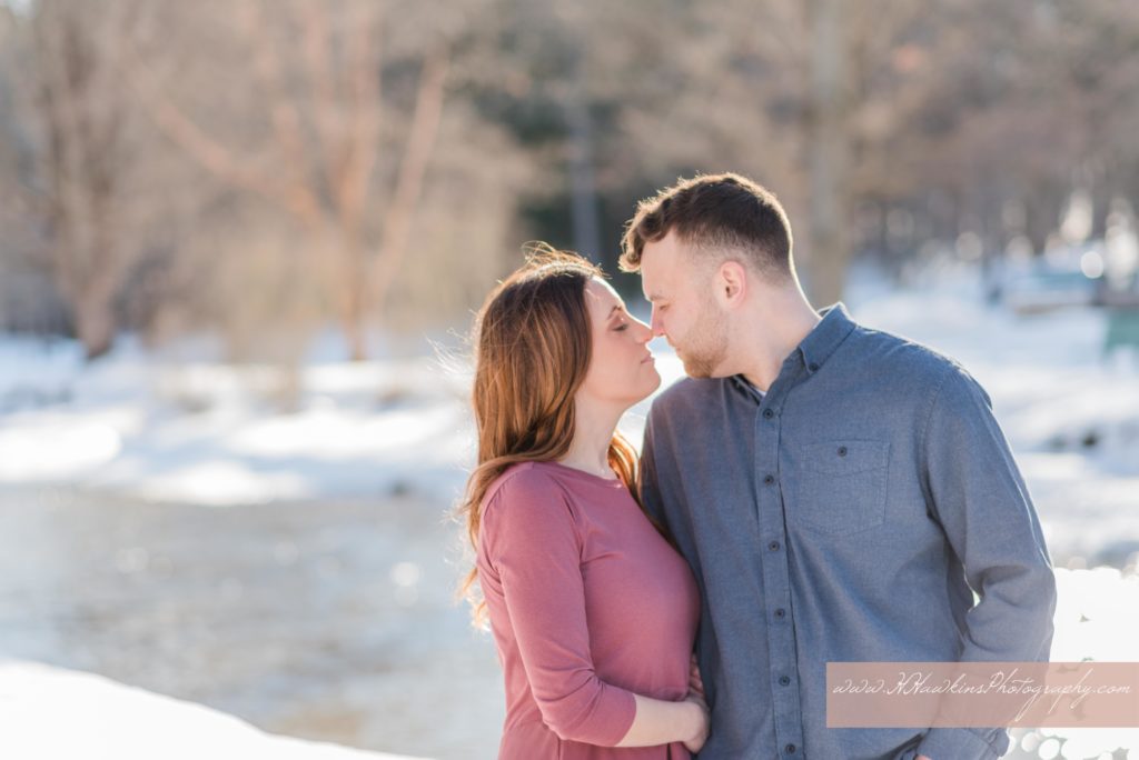 Bride and groom give each other eskimo kisses as they stand in front of a snowy creek of Marcellus Park NY for their engagement pictures