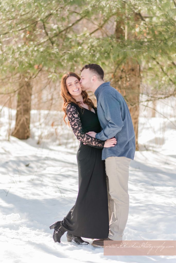 Groom kisses bride in a black dress and lace sleeves on the cheek at Baltimore Woods Marcellus NY