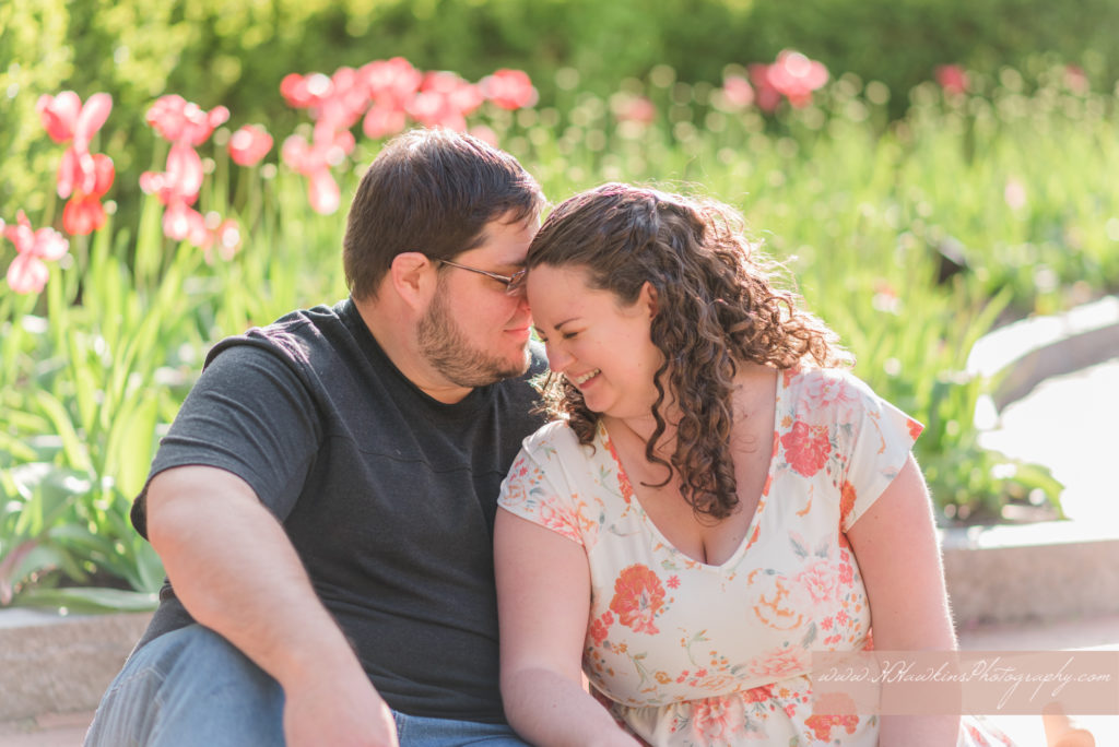 Groom nuzzles in to bride as they sit in front of pink tulips at Franklin Square Park in Syracuse NY during their engagement photos
