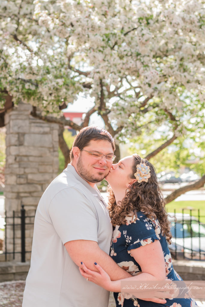 Bride kisses groom on the cheek in front of white spring blossom tree