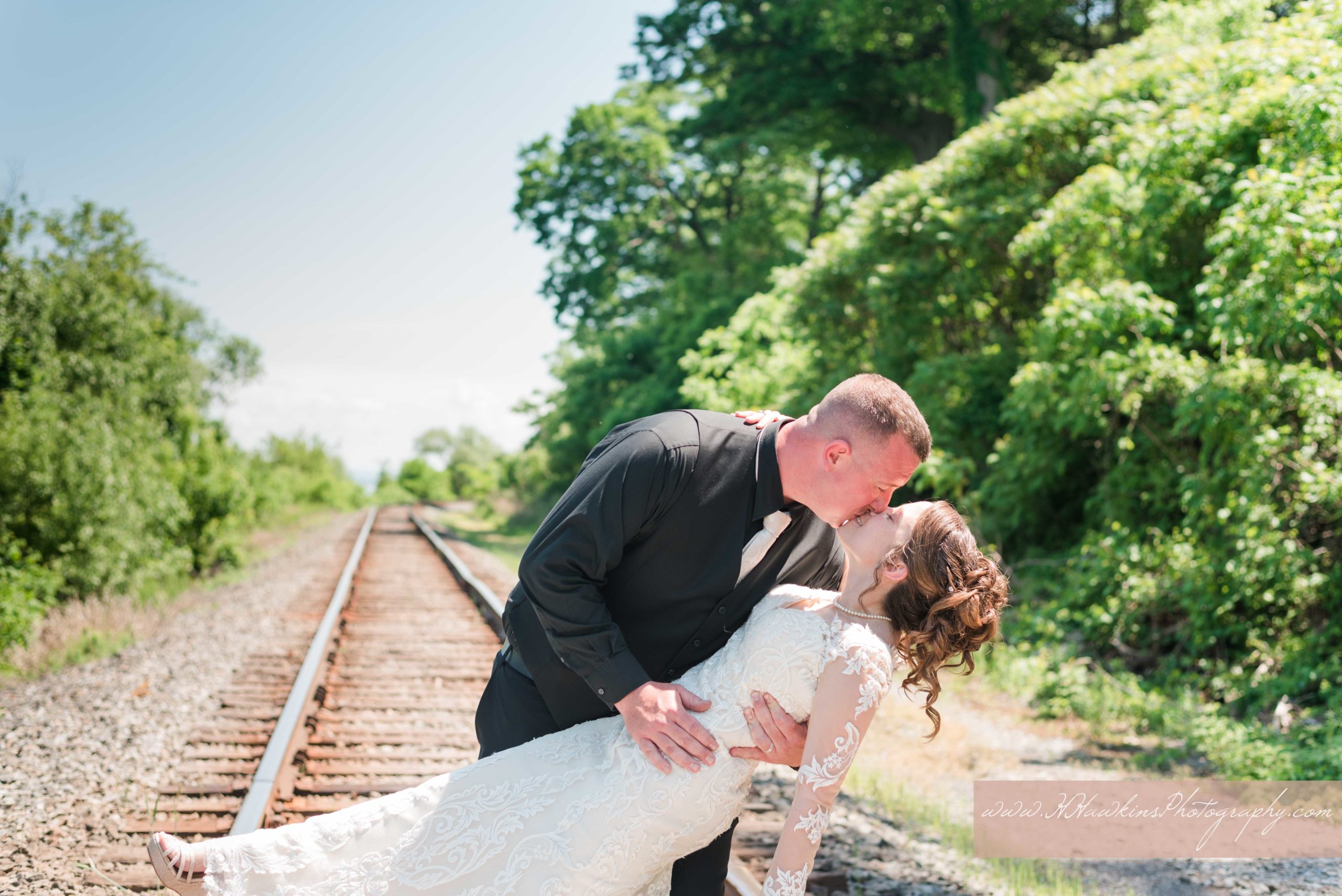 Groom dip kisses bride on the train tracks down by the lake at their Belhurst Castle on the lake wedding