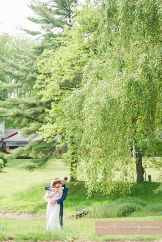 Groom kisses bride on the temple in front of weeping willow tree at Springside Inn Auburn NY for their wedding pictures