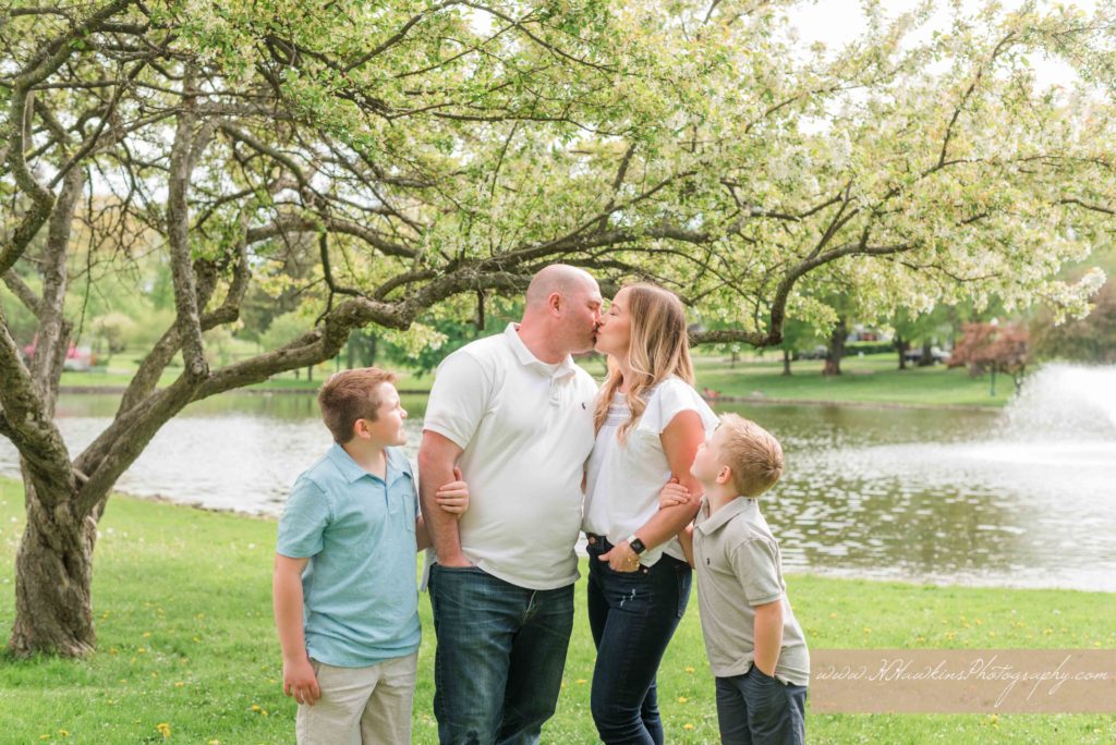 Mom and dad kiss while their boys look on at their extended family session at Hoopes Park Auburn NY by syracuse family photographer