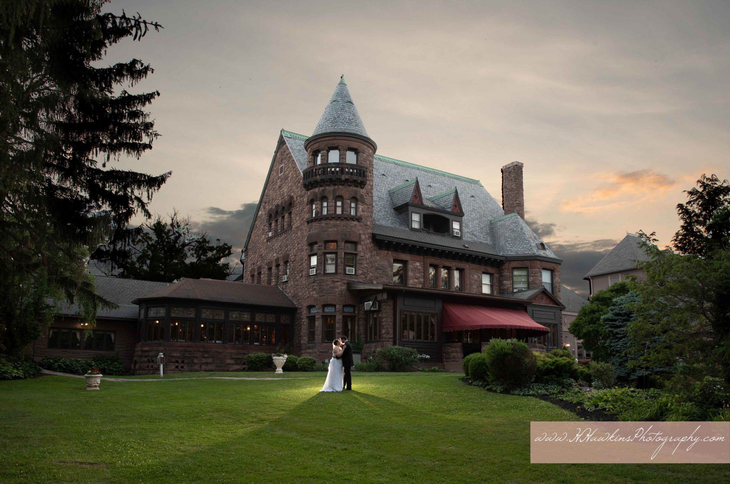 Belhurst Castle with sunset behind bride and groom standing in lawn