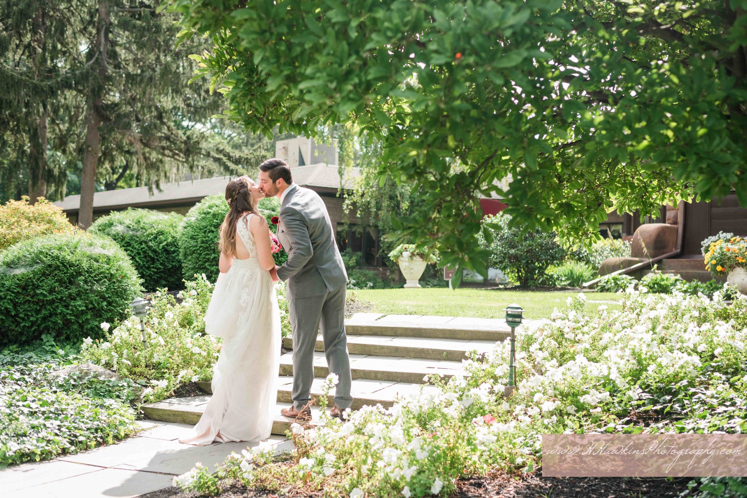 Groom and bride kiss on the steps on the back lawn of Belhurst Castle in GEneva NY
