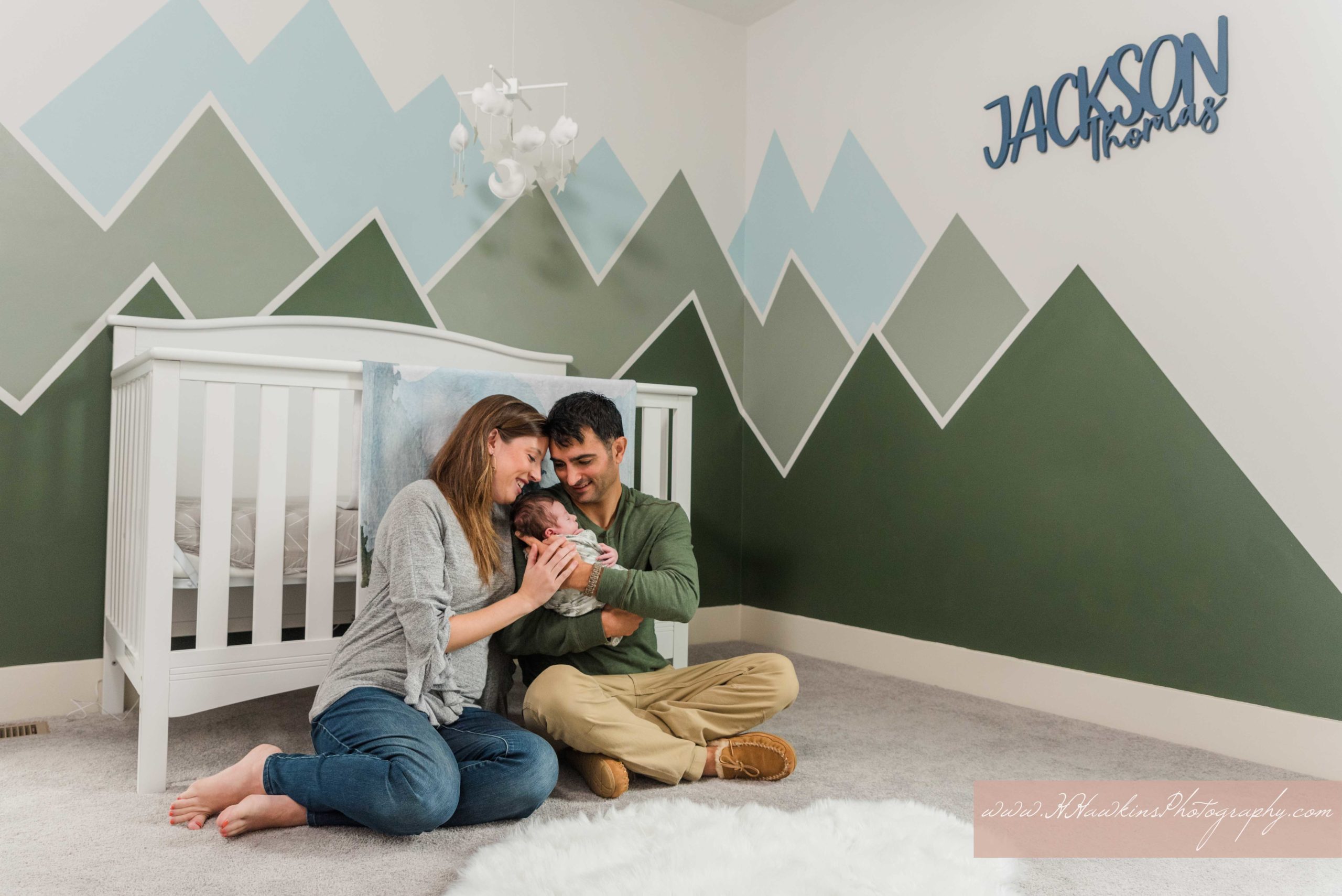 Dad and mom adore newborn baby boy in his green and blue adventure mountain themed nursery