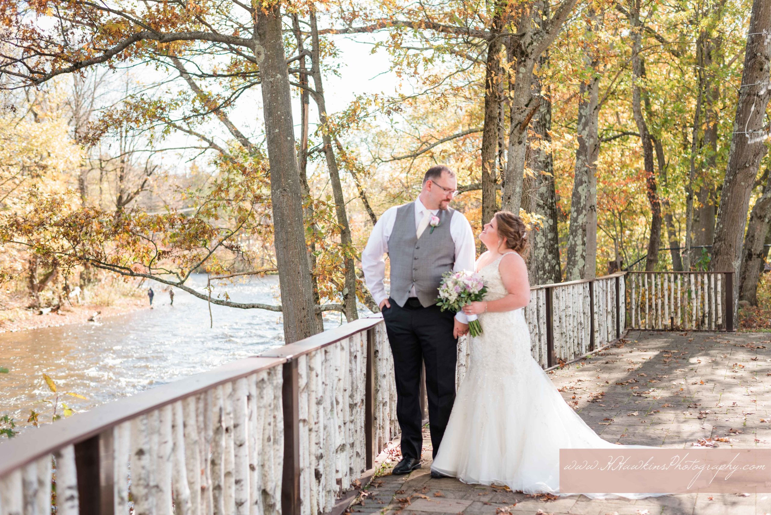 Bride and groom portraits at Tailwater Lodge's ceremony site by Salmon River with white birch railing and autumn leaves