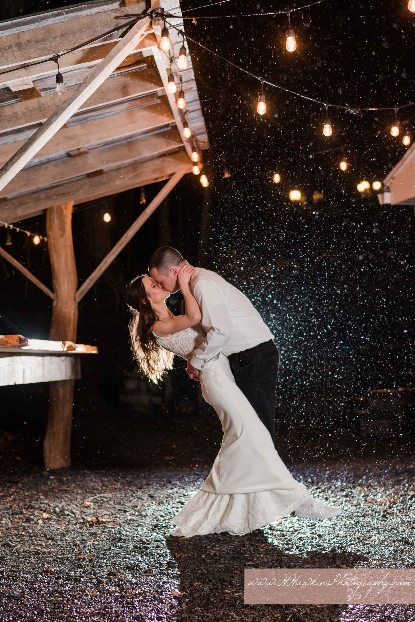 Epic night time shot of bride and groom kissing with backlighting and rain and cafe lights at Springside Inn in Auburn NY by Syracuse photographer