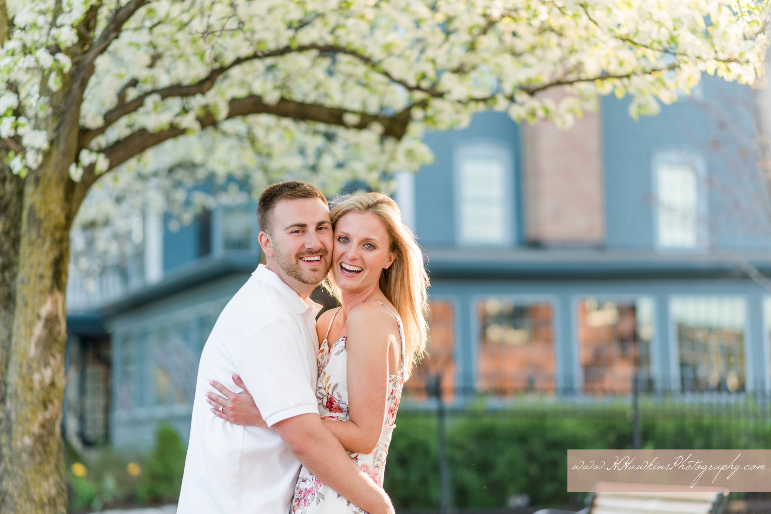 Bride and groom laugh under white blossoming tree outside of the Sherwood Inn during their Skaneateles engagement photos session