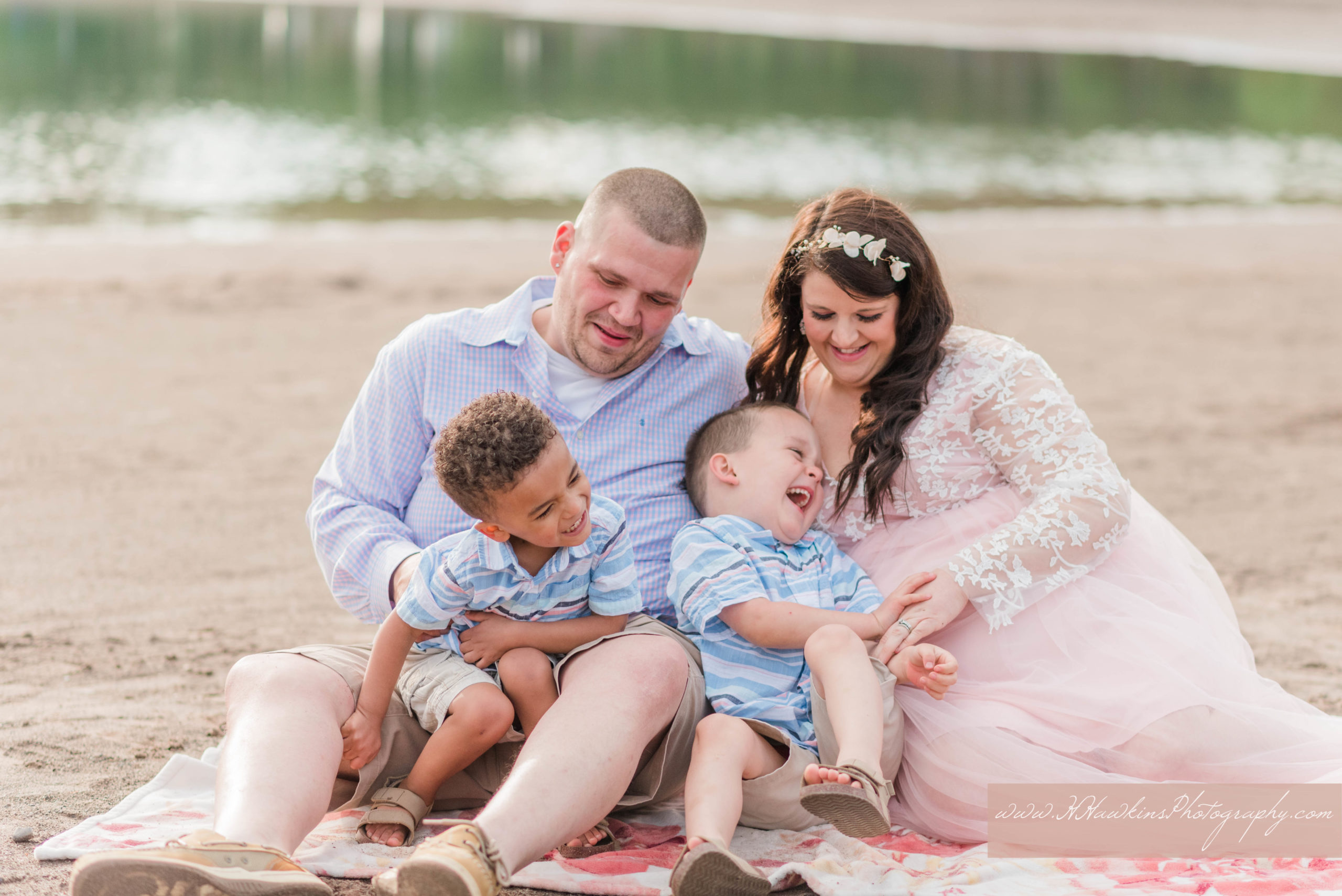 Family of four with pregnant mom sit on the beach at Green Lakes State Park and play together