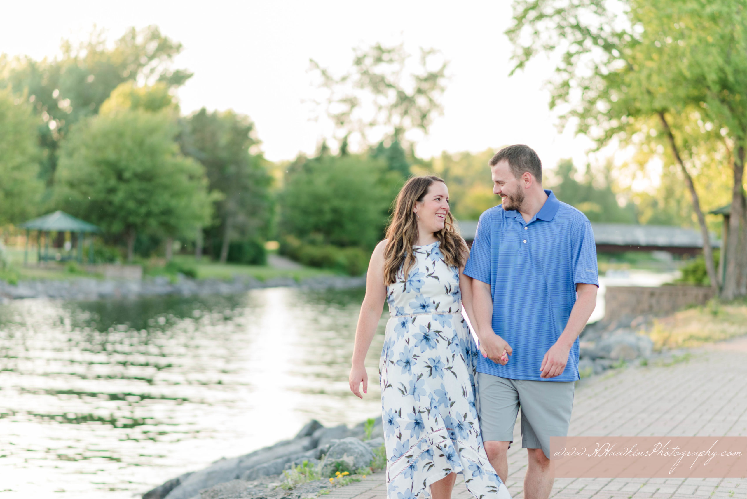 Bride to be in blue floral dress and groom in blue polo have engagement photos taken at Canal at Emerson Park in Auburn NY