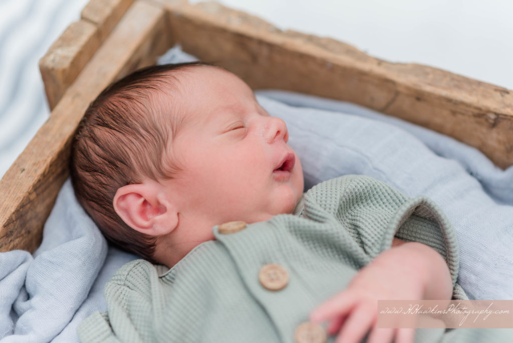 Baby boy in wooden box yawns widely during Syracuse newborn family pictures